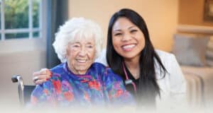 A resident in a wheelchair sitting next to a smiling nurse at the Western Slope Health facility